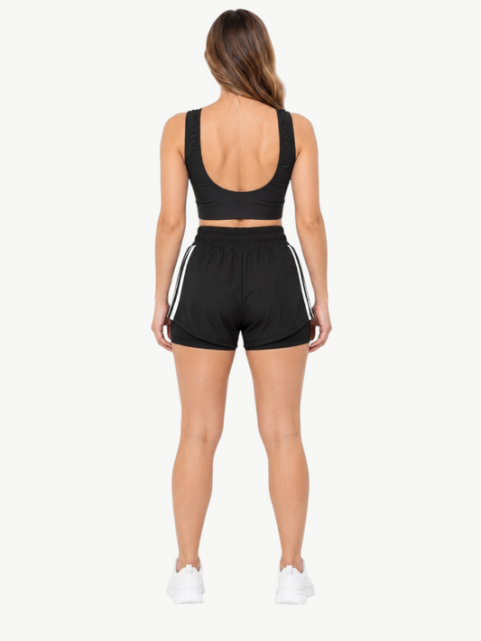 Back view of a woman wearing a black JM Brazilian Activewear 2-in-1 short set with a crop top and layered shorts.