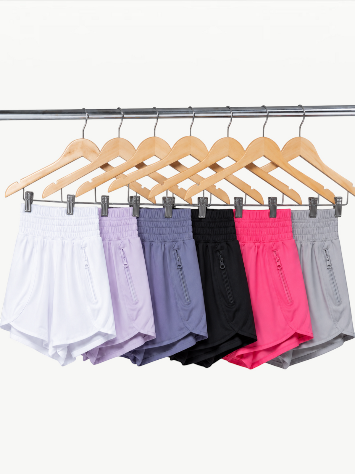 JM Brazilian Activewear 2-in-1 athletic shorts in white, lavender, blue, black, pink, and grey on wooden hangers