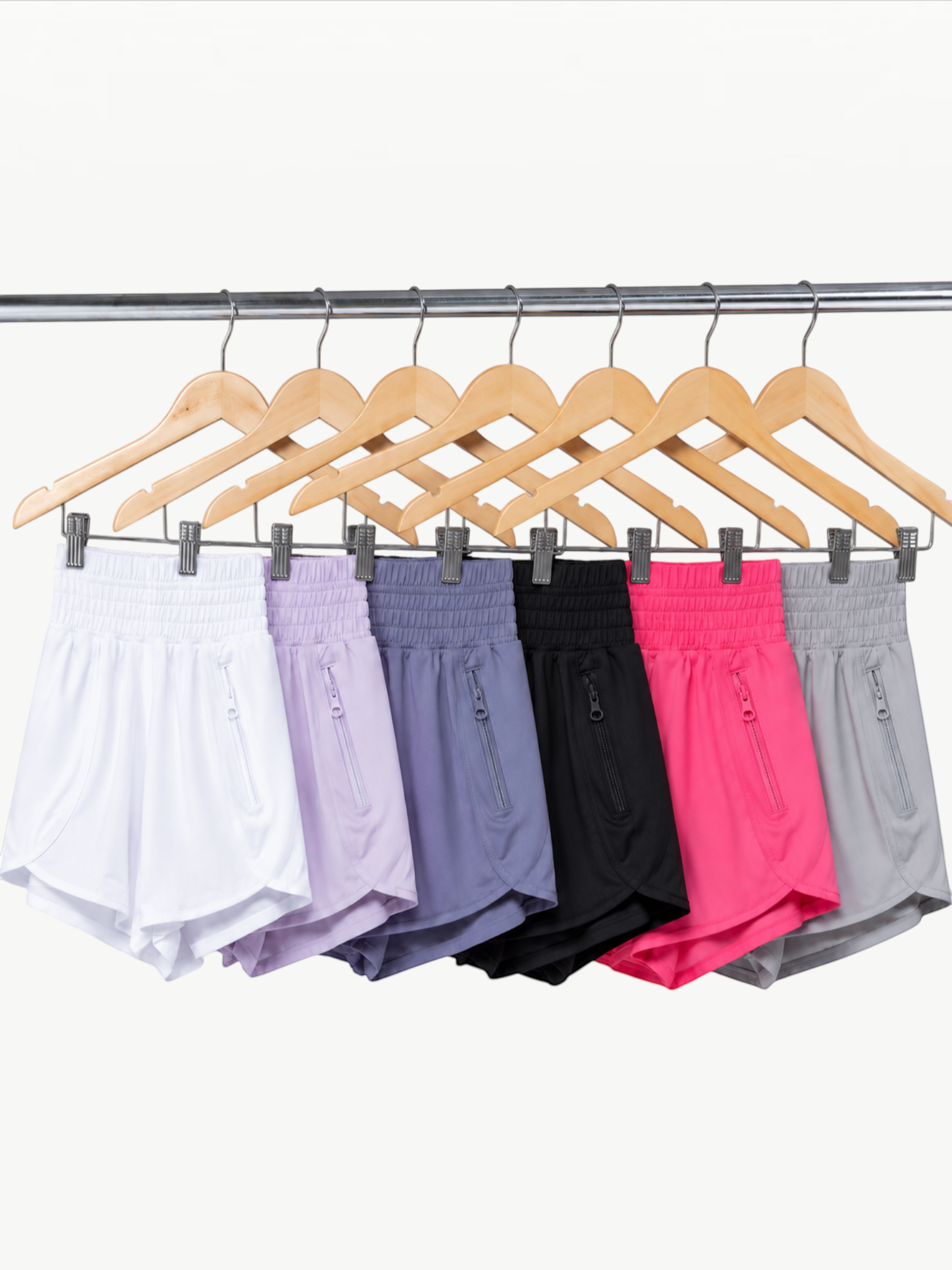 JM Brazilian Activewear 2-in-1 athletic shorts in white, lavender, blue, black, pink, and grey on wooden hangers