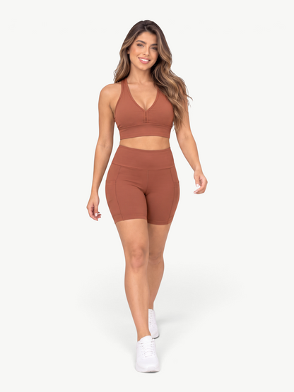 Model wearing JM Brazilian Activewear brown high-waisted biker shorts with side pockets and a matching sports bra.