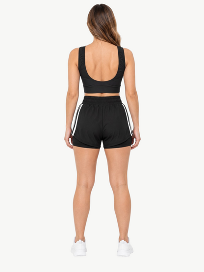 Back view of a woman wearing a black JM Brazilian Activewear 2-in-1 short set with a crop top and layered shorts.
