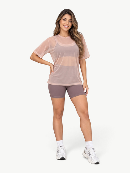 Model wearing a JM Brazilian Activewear sheer blush pink mesh t-shirt over a sports bra and athletic shorts