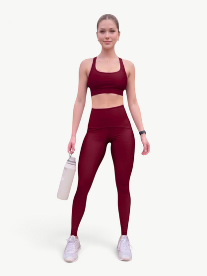 Model wearing a JM Brazilian Activewear burgundy high-waisted legging set with a strappy-back sports bra