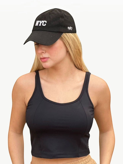 Modelo loira vestindo o Dallas Crop Top preto da JM Brazilian Activewear com boné preto estilo casual