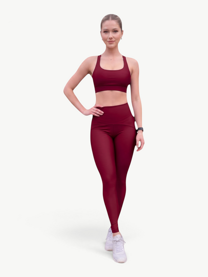 Model wearing a JM Brazilian Activewear dark red two-piece legging set with a strappy-back top and high-waisted leggings.