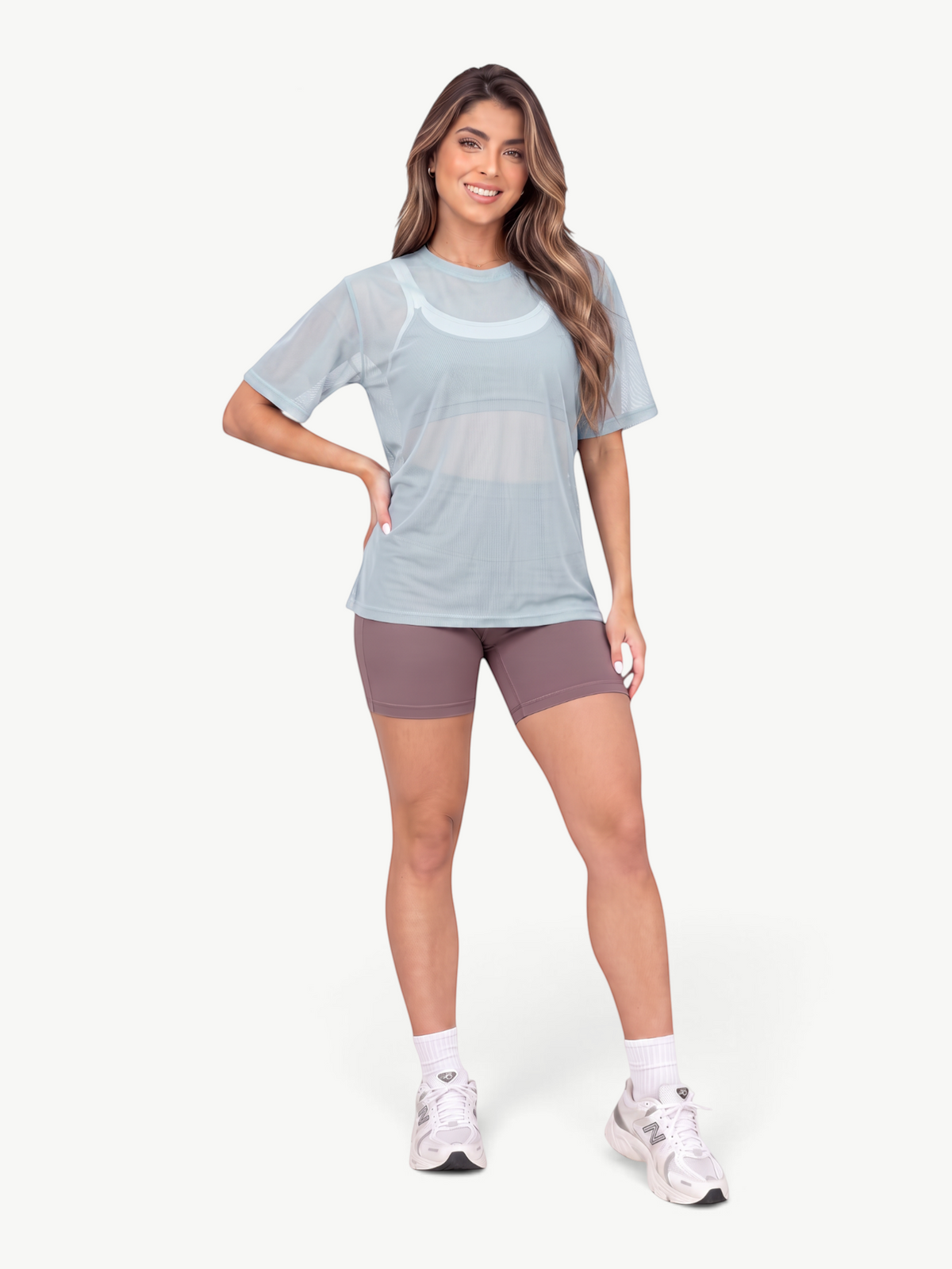 Model wearing a light blue JM Brazilian Activewear mesh t-shirt over a sports bra with mauve shorts and sneakers.