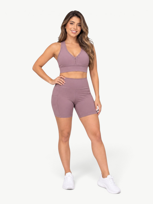 Model wearing JM Brazilian Activewear mauve high-waisted biker shorts with side pockets and a matching sports bra.
