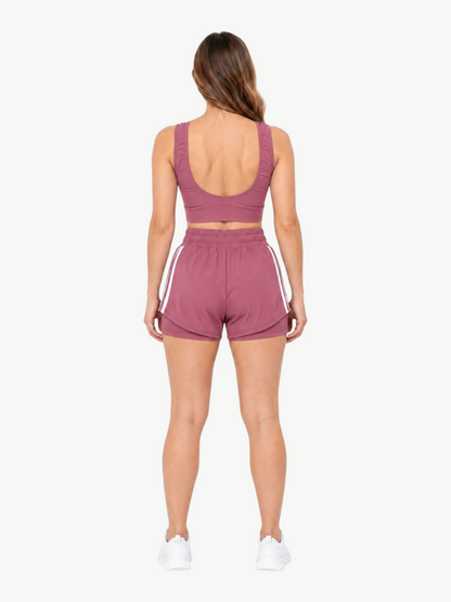 Back view of a woman wearing a mauve JM Brazilian Activewear 2-in-1 short set with a crop top and layered shorts.