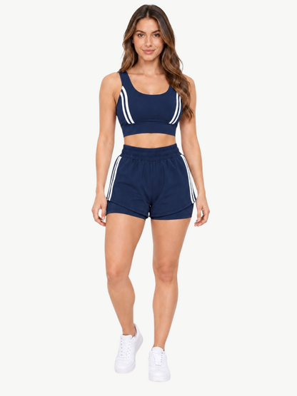 Model wearing a JM Brazilian Activewear navy blue 2-in-1 short set with white side stripes and a supportive crop top.