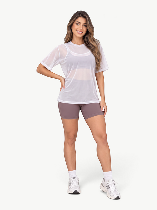 Model wearing a white JM Brazilian Activewear sheer mesh t-shirt over a black sports bra and mauve athletic shorts.